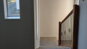 Una escalera con barandilla de madera y pasamanos de metal negro, que conduce a un rellano con una araña.