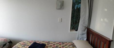 Un dormitorio con una cama, una ventana con cortinas, una lámpara de pared y un pequeño marco de fotos.