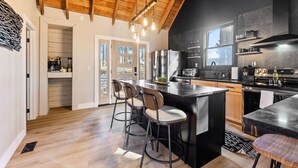 Una cocina moderna con techo de madera, encimeras negras y electrodomésticos de acero inoxidable. Hay tres taburetes de bar y una isla grande.