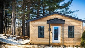 Une petite cabane en bois avec un toit à pignon, une porte d’entrée et deux fenêtres.