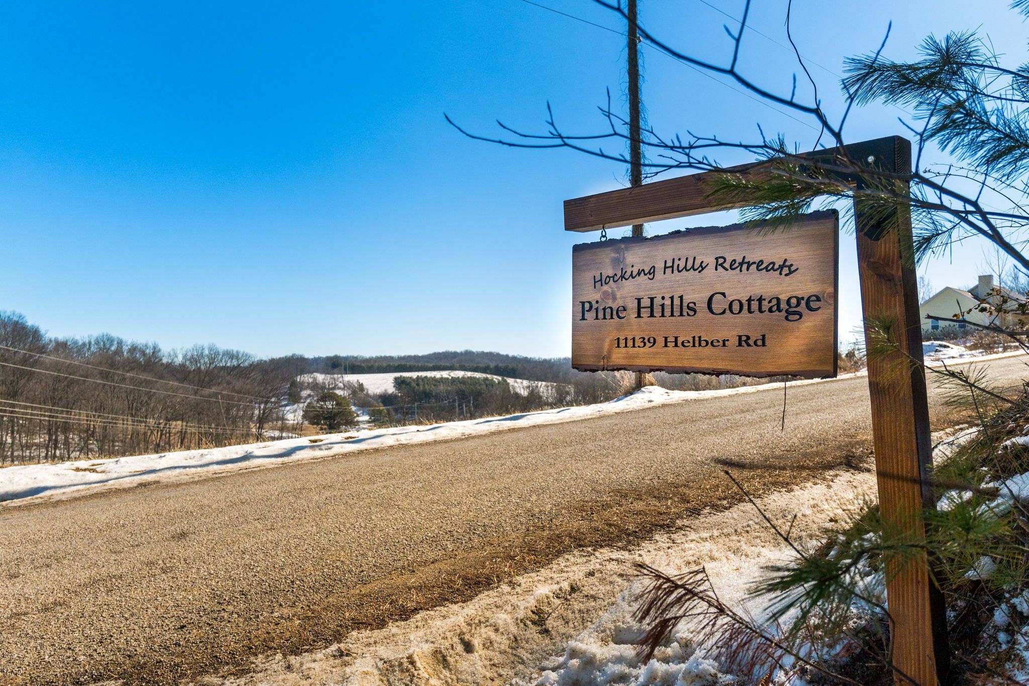 Un panneau en bois indiquant l’emplacement de « Hocking Hills Retreats, Pine Hills Cottage », situé au 11139, Helber Rd.