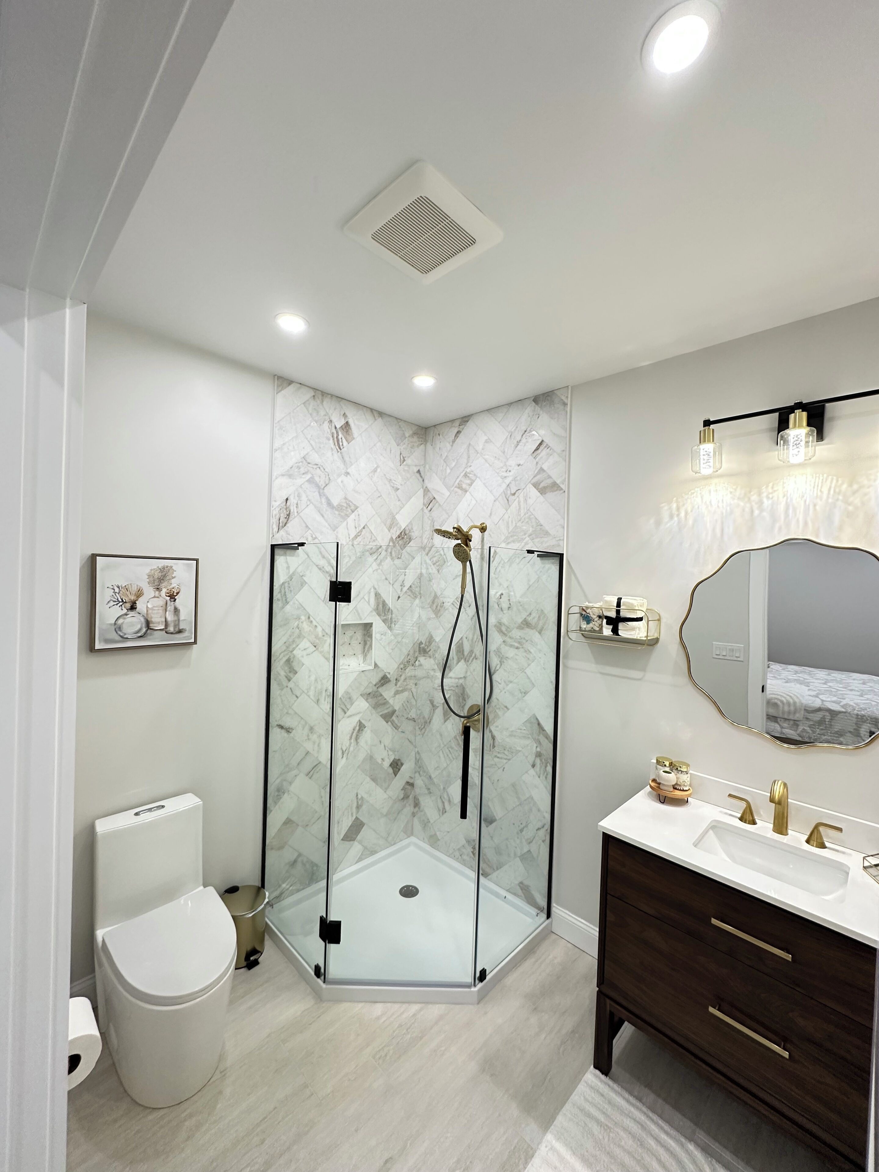 Un baño moderno con cabina de ducha acristalada, inodoro blanco, tocador de madera oscura y pared con estampado de mármol.