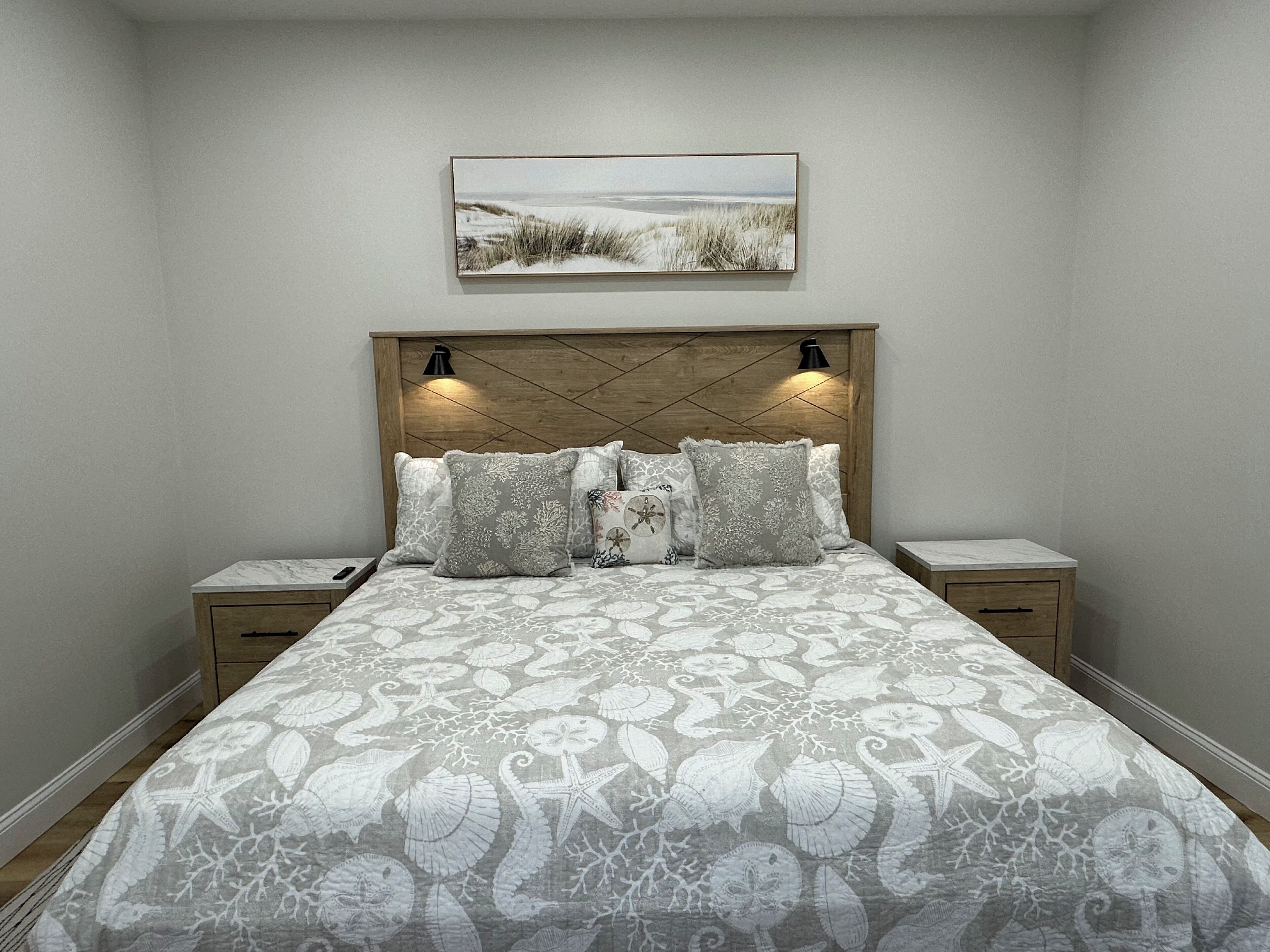 A bedroom with a bed, nightstands, a wooden headboard, and a framed picture on the wall.