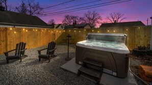 Un patio trasero con un jacuzzi, dos sillas Adirondack y una valla de madera.
