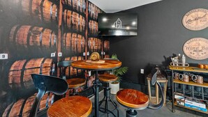 Zona de bar con decoración temática de barriles de madera, un televisor montado en la pared y una barra con diversos botellas y vasos.