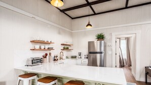A modern kitchen with a large island, bar stools, stainless steel appliances, and wooden shelves.