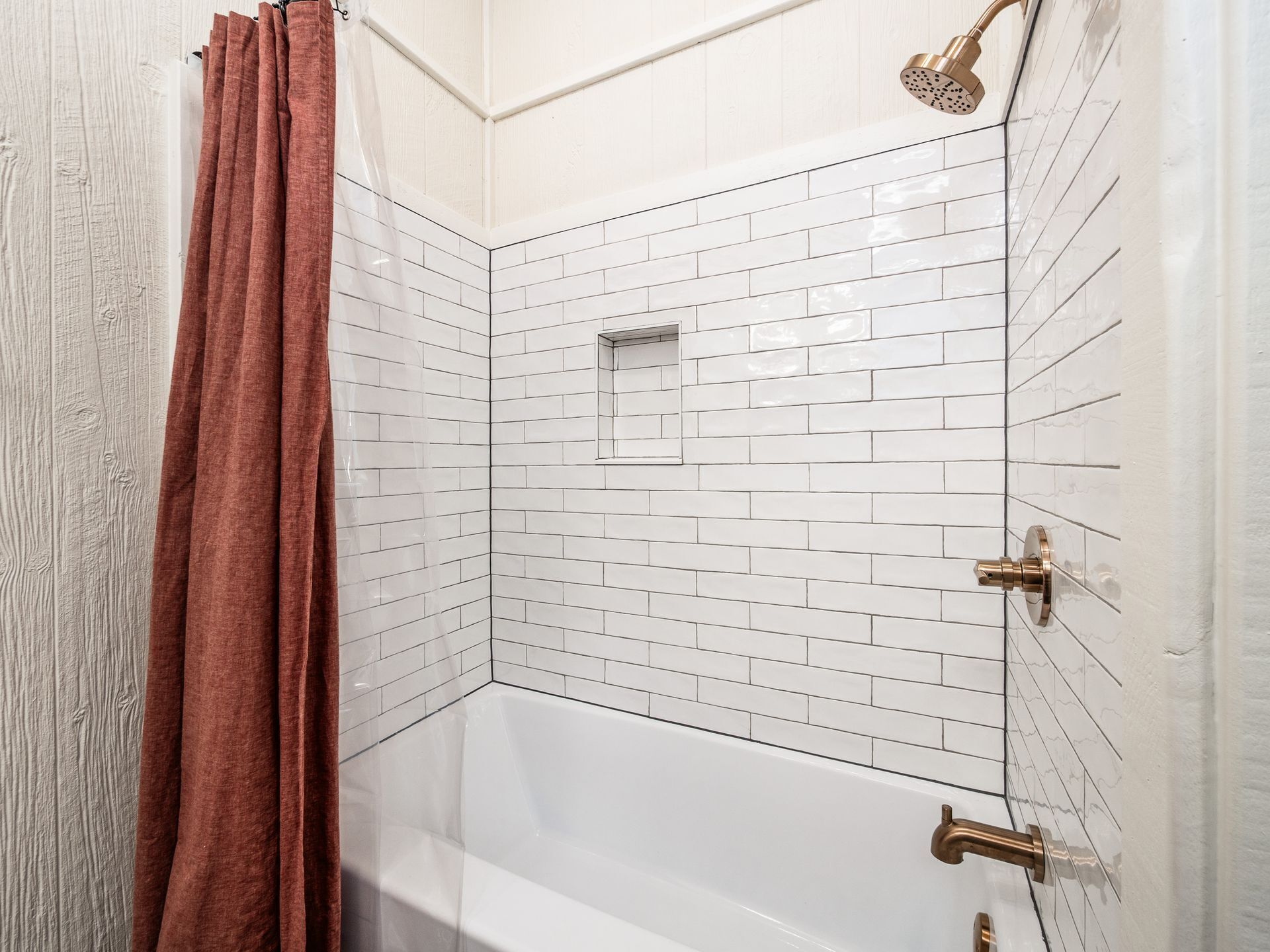 A corner shower with white tiled walls and a clear glass door.