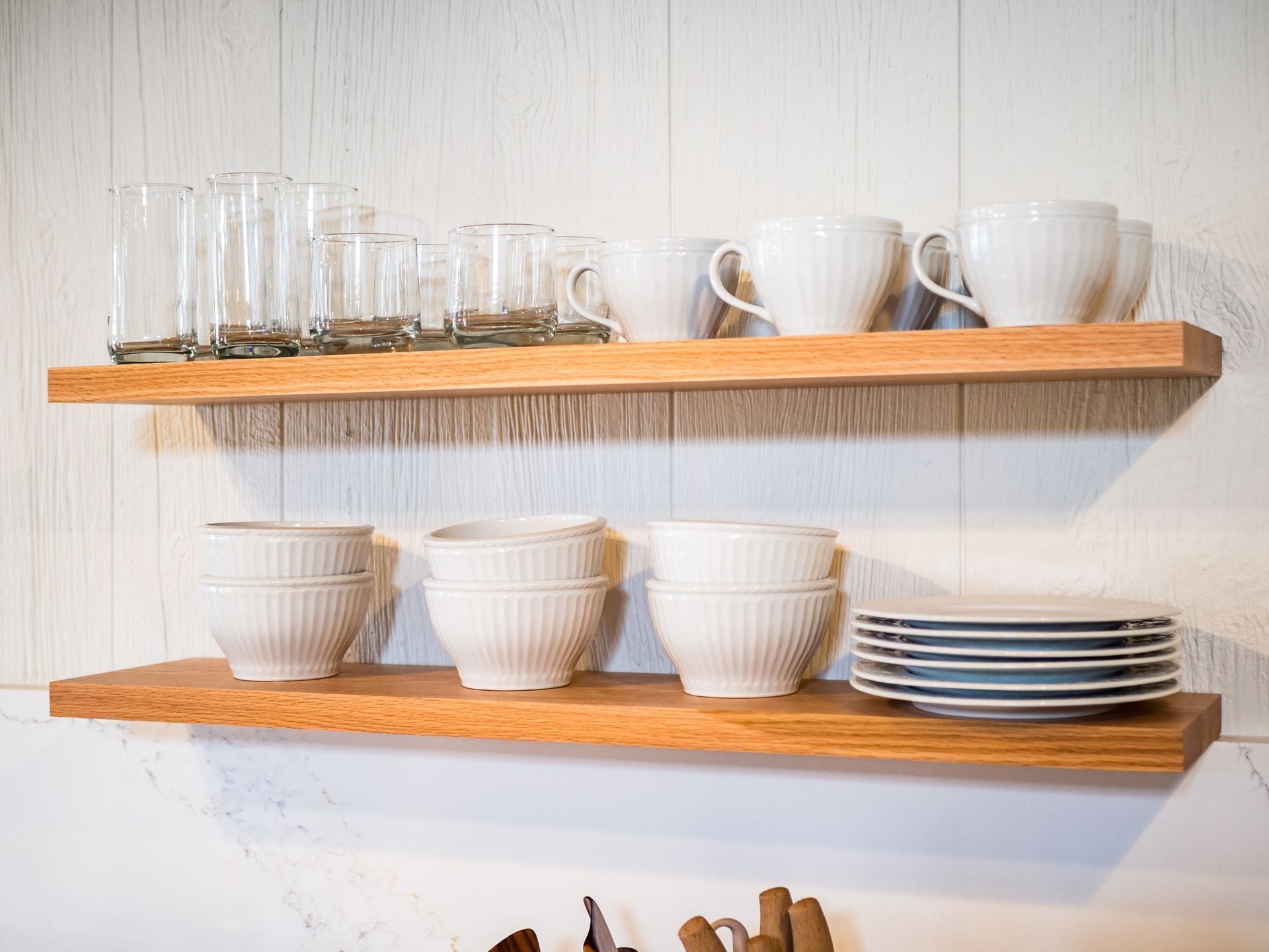 Una cocina con repisas de madera que sostienen cristalería y vajilla de cerámica blanca.