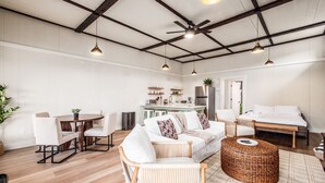 A spacious living area with a dining table, a sofa, and a bed. There is a kitchen in the background with a refrigerator and a sink.