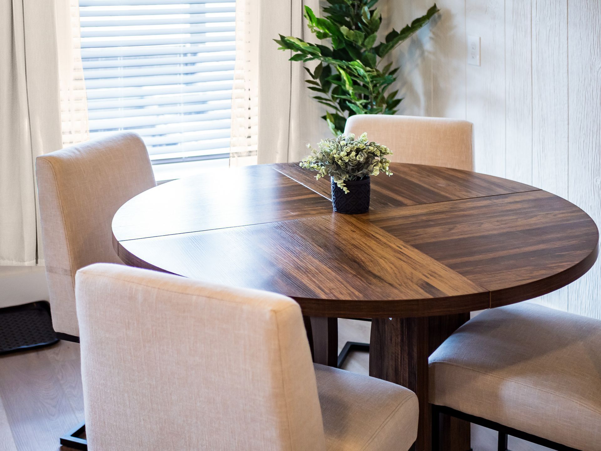 A round wooden dining table with a potted plant in the center, surrounded by four upholstered chairs.