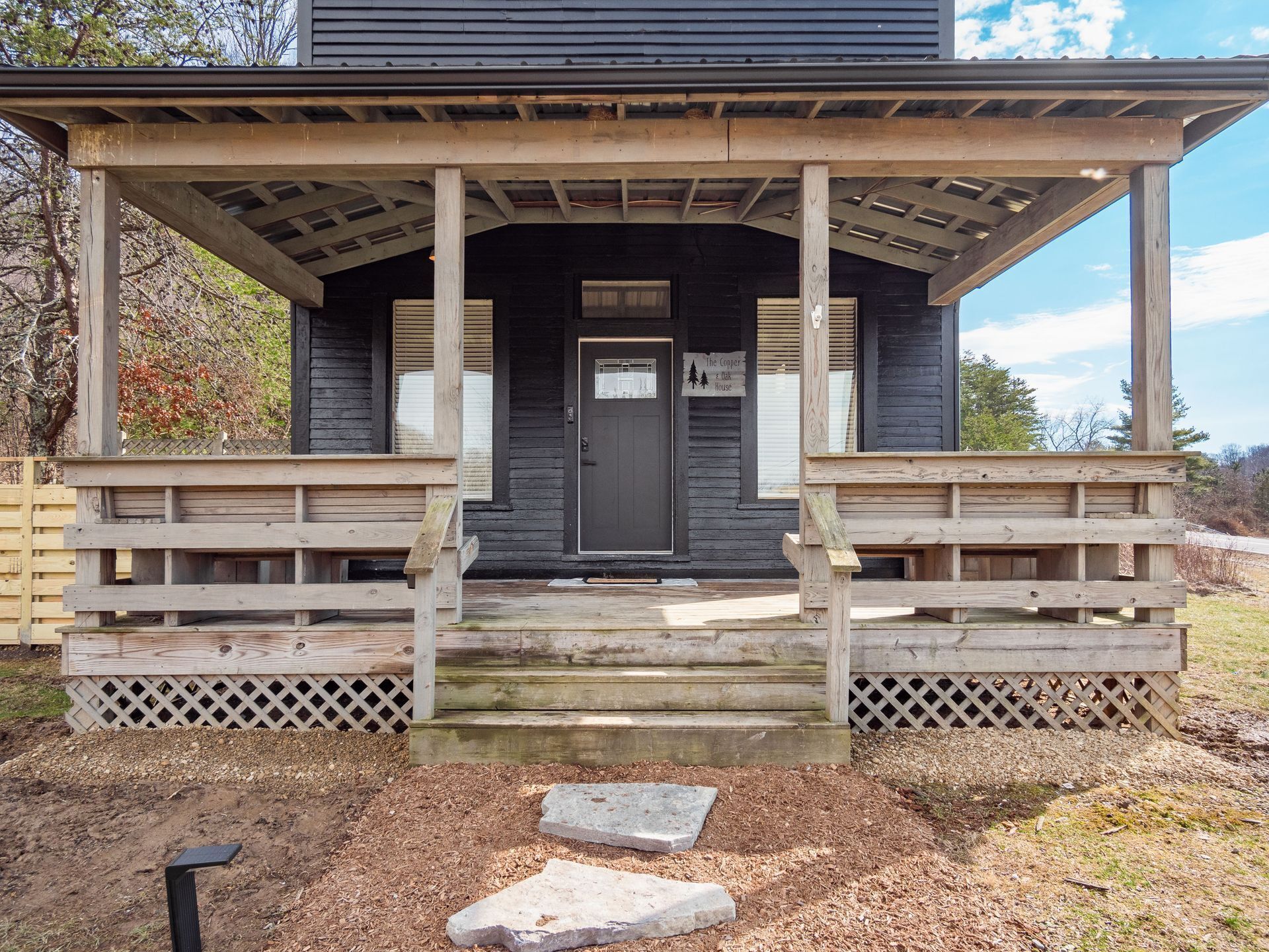 A wooden porch with a dark door, wooden railings, and a lattice base.