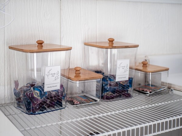 Three glass jars with wooden lids on a white shelf. Each jar has a label with text and a floral design.