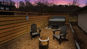Un área de patio al aire libre con sillas Adirondack, un pozo de fuego y un jacuzzi.