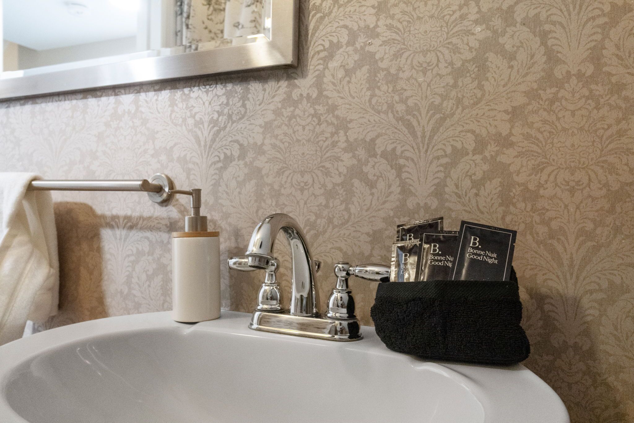 A bathroom sink with a modern faucet, a towel rack, and a black soap dispenser.