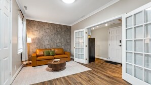 Uma sala de estar moderna com piso de madeira, sofá de couro com almofadas, mesa de centro redonda e parede com textura.