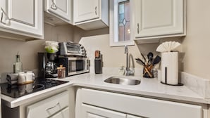 Uma cozinha moderna com armários brancos, forno embutido, micro-ondas, cafeteira e pia.