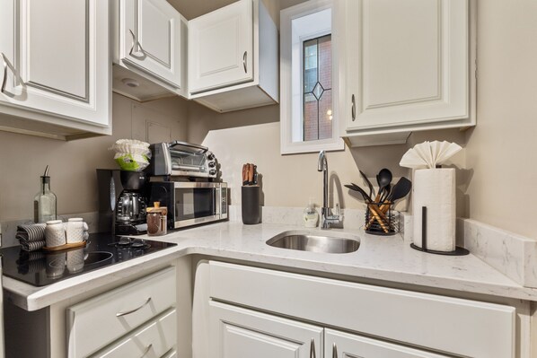 A modern kitchen with white cabinets, a built-in oven, a microwave, a coffee maker, and a sink. - Nightingale Cottage - Near NCH! (Columbus)