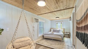 A bedroom with a bed, a hanging chair, a bedside table, and a wall-mounted air conditioner.