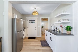 Una cocina moderna con refrigerador, armarios blancos, encimera negra y lámpara colgante.