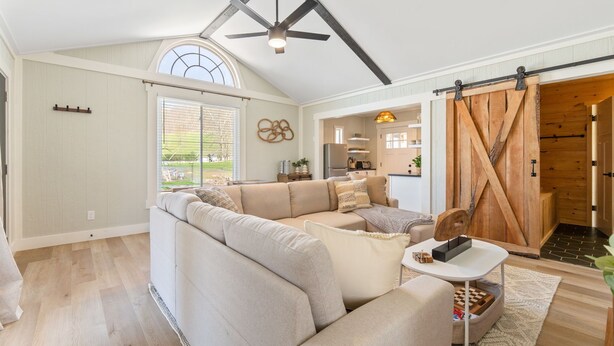 A spacious living room with a large sectional sofa, a ceiling fan, and a sliding barn door leading to a kitchen.