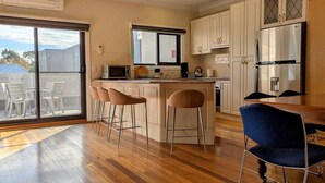 A modern kitchen with a central island, bar stools, a dining table with chairs, and a large refrigerator. - Heart of Surrey Hills (Parking On Request) (Surrey Hills)