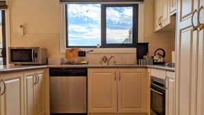 A kitchen with white cabinets, a dishwasher, a stove, a microwave, and a window with a view of the sky. - Heart of Surrey Hills (Parking On Request) (Surrey Hills)