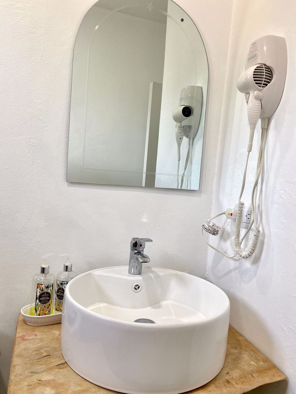 A bathroom with a white sink, a mirror, and a hairdryer mounted on the wall.