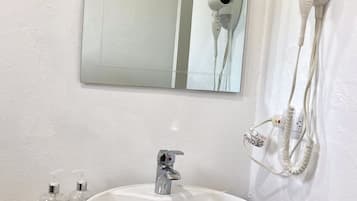 A bathroom with a white sink, a mirror, and a hairdryer mounted on the wall.