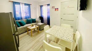 A compact living space with a kitchenette, a sofa with teal cushions, a small table with chairs, and a TV mounted on the wall. - Cape Coral 1 (Cabrera)