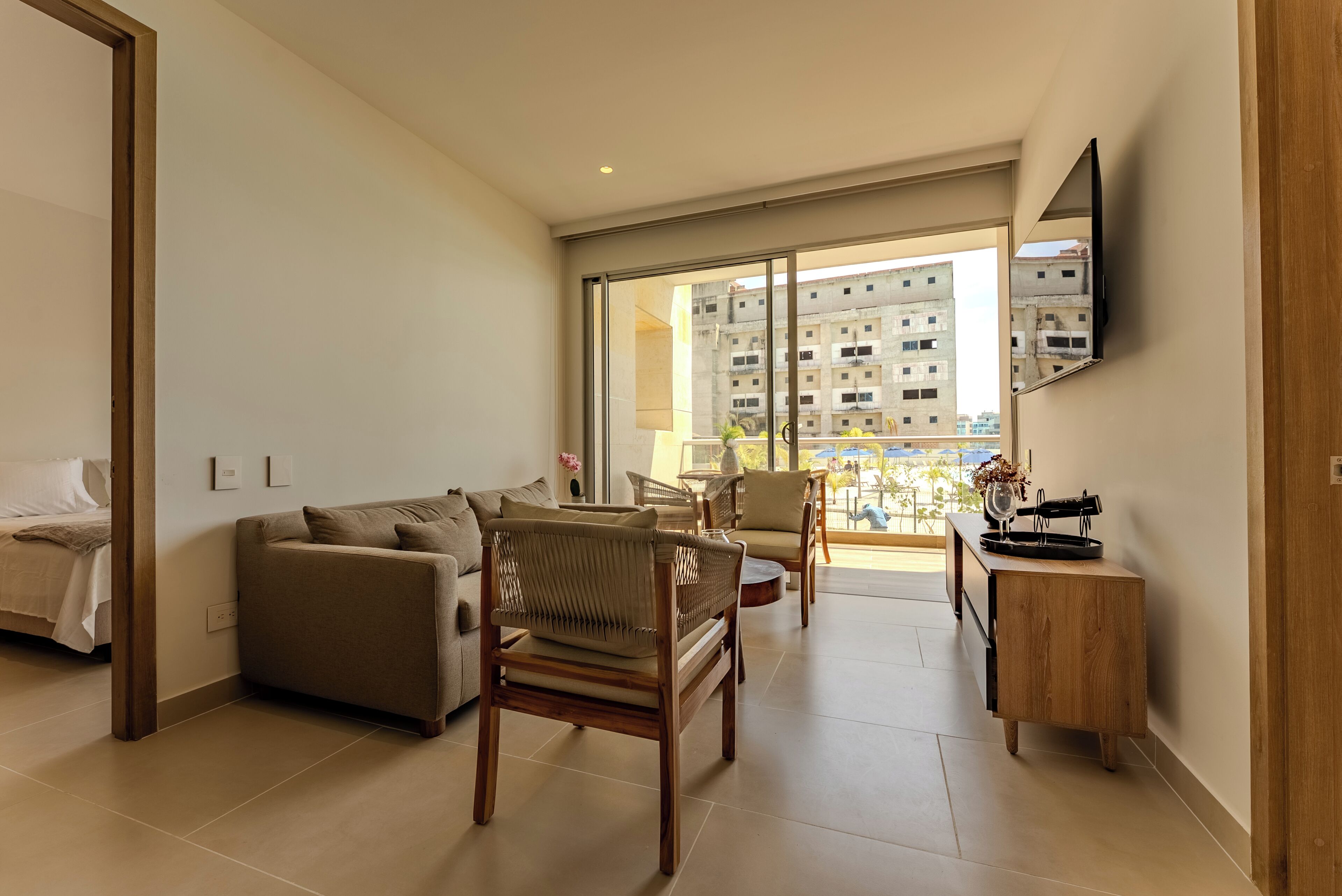 A modern living room with a sofa, chairs, a wooden side table, and a large window with a view of buildings.