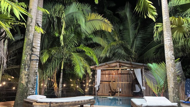 Una terraza de madera con dos sillones de descanso, una piscina y una cabaña de madera con toldo.