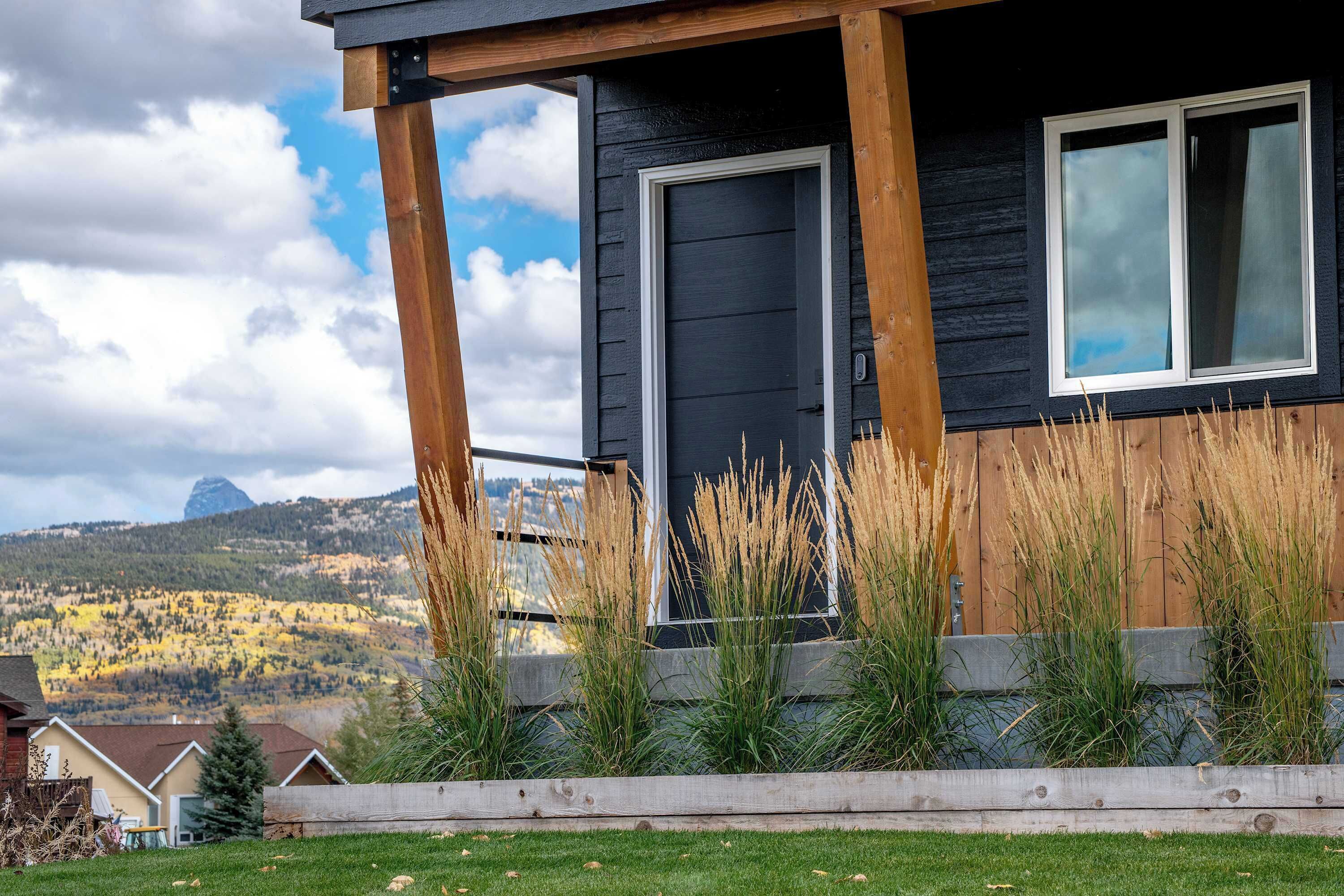 A modern house with a dark exterior, a wooden porch, and a view of a mountain range.