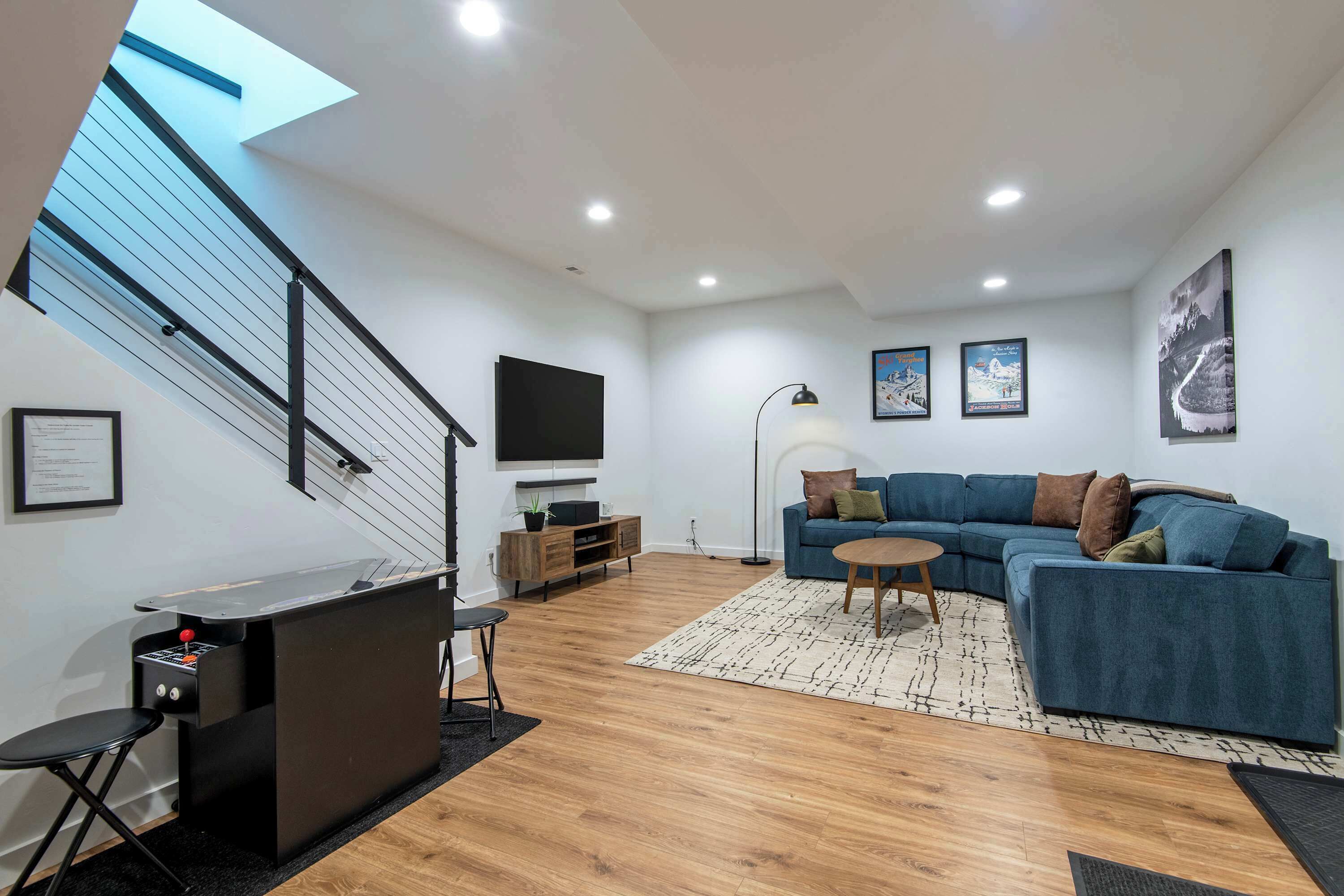Een moderne woonkamer met een blauwe bank, een houten salontafel, een bureau met een computer en een trap met dakraam.