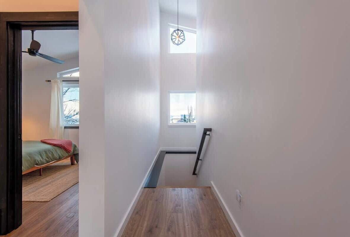 A narrow hallway with a wooden floor, a bed with a green bedspread in the background, and a ceiling fan.