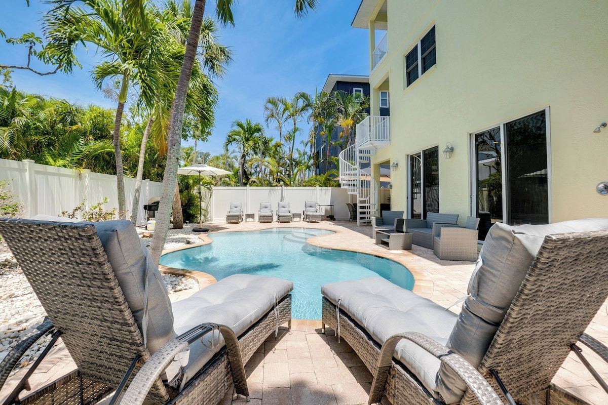 A swimming pool with lounge chairs, a white fence, and palm trees.