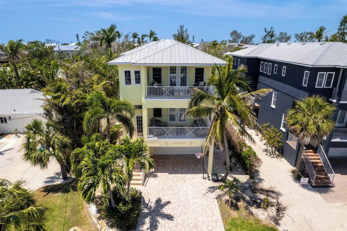 A two-story building with a balcony, surrounded by palm trees and a paved walkway.