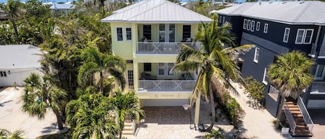 A two-story building with a balcony, surrounded by palm trees and a paved walkway.