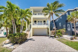 A two-story building with a covered driveway, palm trees, and a clear sky. - Island Dream (Anna Maria)