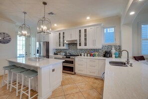 A modern kitchen with white cabinetry, a central island with bar stools, stainless steel appliances, and pendant lighting. - Island Dream (Anna Maria)