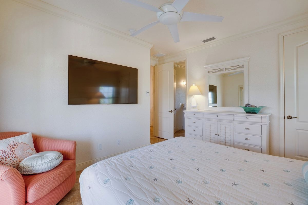 A bedroom with a bed, a ceiling fan, a dresser, a mirror, and a door leading to another room.