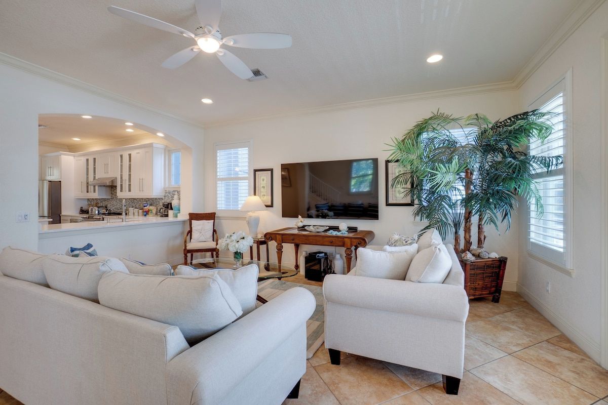 A living room with a sofa, armchairs, a coffee table, a TV, a ceiling fan, and a large potted plant.