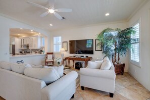 A living room with a sofa, armchairs, a coffee table, a TV, a ceiling fan, and a large potted plant.