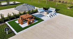 A patio area with a picnic table, benches, a fire pit, and a striped umbrella.