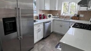 Una cocina moderna con armarios blancos, electrodomésticos de acero inoxidable y piso de baldosas.