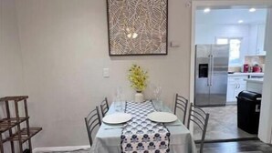 Un comedor con una mesa dispuesta para dos, un adorno en la pared y una cocina visible a través de un umbral abierto.