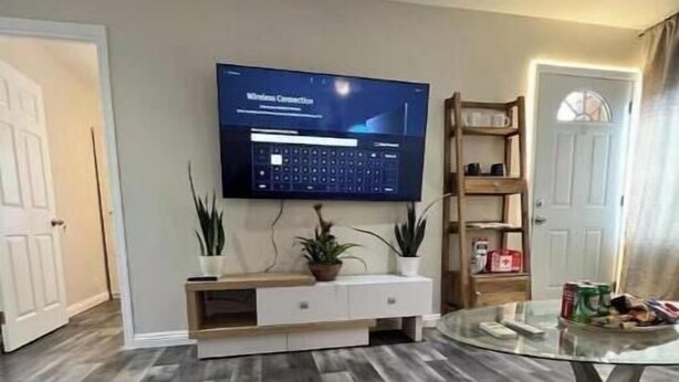 Una sala de estar moderna con un televisor de pantalla plana montado en la pared, un mueble de entretenimiento de madera debajo, una mesa de centro de vidrio y piso de madera oscura.
