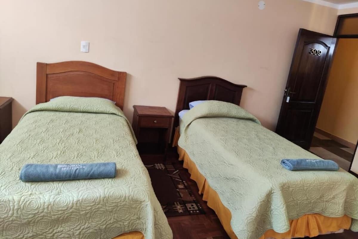 Una habitación con dos camas individuales, cabeceros de madera, una mesita de noche y una puerta con placa de número.