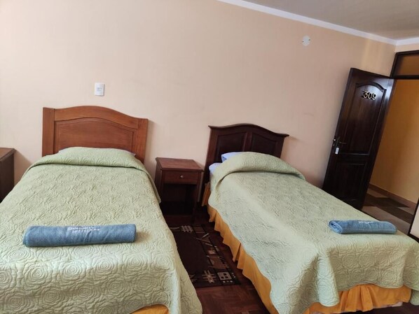 A room with two single beds with wooden headboards, a nightstand, and a door with a number plate. - HOTEL BENELUX (La Paz)
