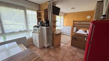 Een compacte kamer met een bed, een kleine kitchenette, een televisie en een raam met gordijnen.