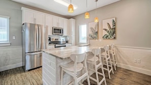 A modern kitchen with white cabinetry, stainless steel appliances, a marble island, and bar stools. - Sleeps 33! 4 Condos, Walk to the Beach, Resort-style Pool, Endless Summer Resort (Port Aransas)